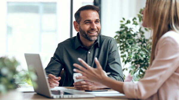 a man and a woman talking at desk with a laptop on it